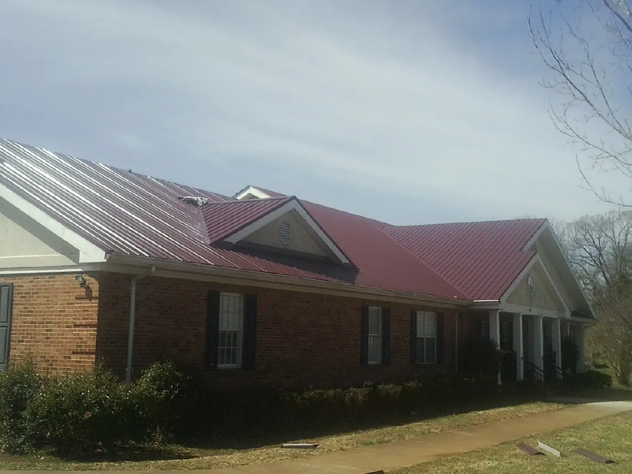 Red metal roof with gabled entries on a long brick building, from a Hail Damage Roof Repair job in Waxahachie