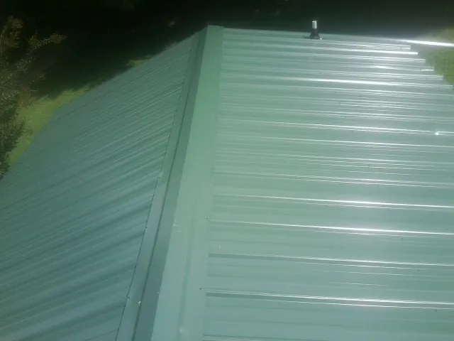 New green metal panels meeting at the ridge of a roof — Flat Roof Repair work by our crew in Waxahachie