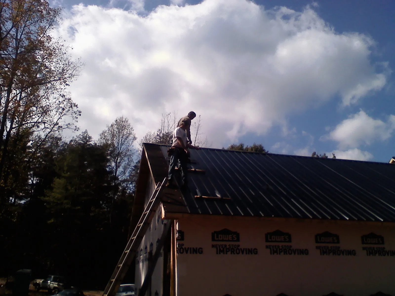 Roofer fastening dark metal panels high against a cloudy sky, from a Roof Inspection job in Waxahachie