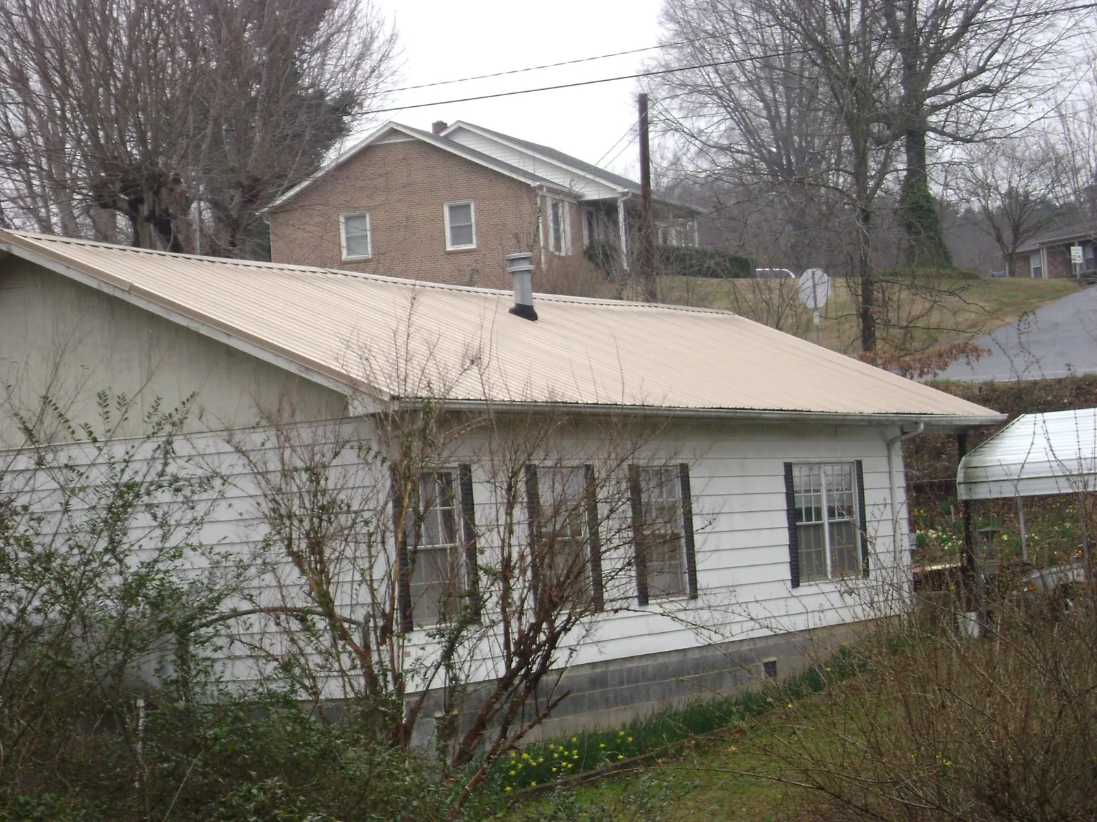 Tan metal roof on a white sided house set into a hillside — Commercial Roofing by Roofing Brothers in Waxahachie